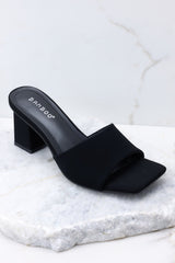 Outer-side view of these heels that feature a square toe, a thick strap across the top of the foot, a block heel, a suede feel, and a slip-on design.