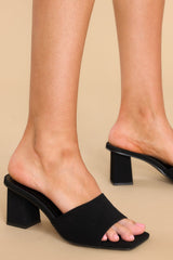 Close up view of these heels that feature a square toe, a thick strap across the top of the foot, a block heel, a suede feel, and a slip-on design. 