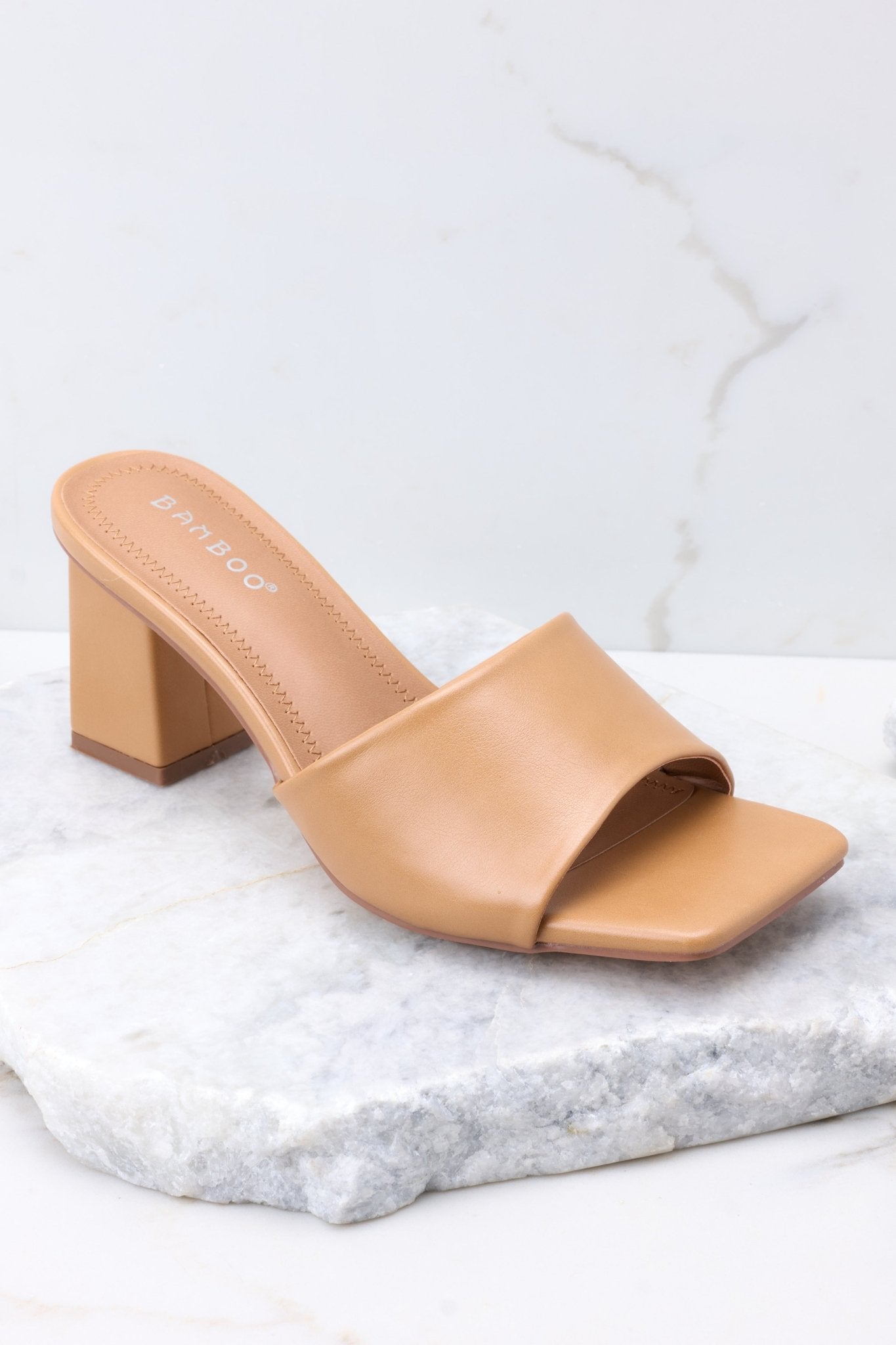 Close up view of these heels that feature a square toe, a thick strap across the top of the foot, a square heel, a faux-leather finish , and a slip-on design. 