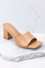 Close up view of these heels that feature a square toe, a thick strap across the top of the foot, a square heel, a faux-leather finish , and a slip-on design. 