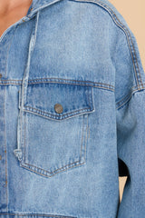 Close up view of this jacket that features a cropped fit, buttons down the front, a hood, and functional pockets.