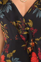 Close up view of this dress that features a v-neckline with a snap button closure, adjustable straps, a self-tie in the back, a side zipper, ruffle detailing, and a wide slit up the leg.