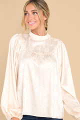 This all ivory satin top features a high neckline with buttons on the side, balloon sleeves, and elastic cuffs.