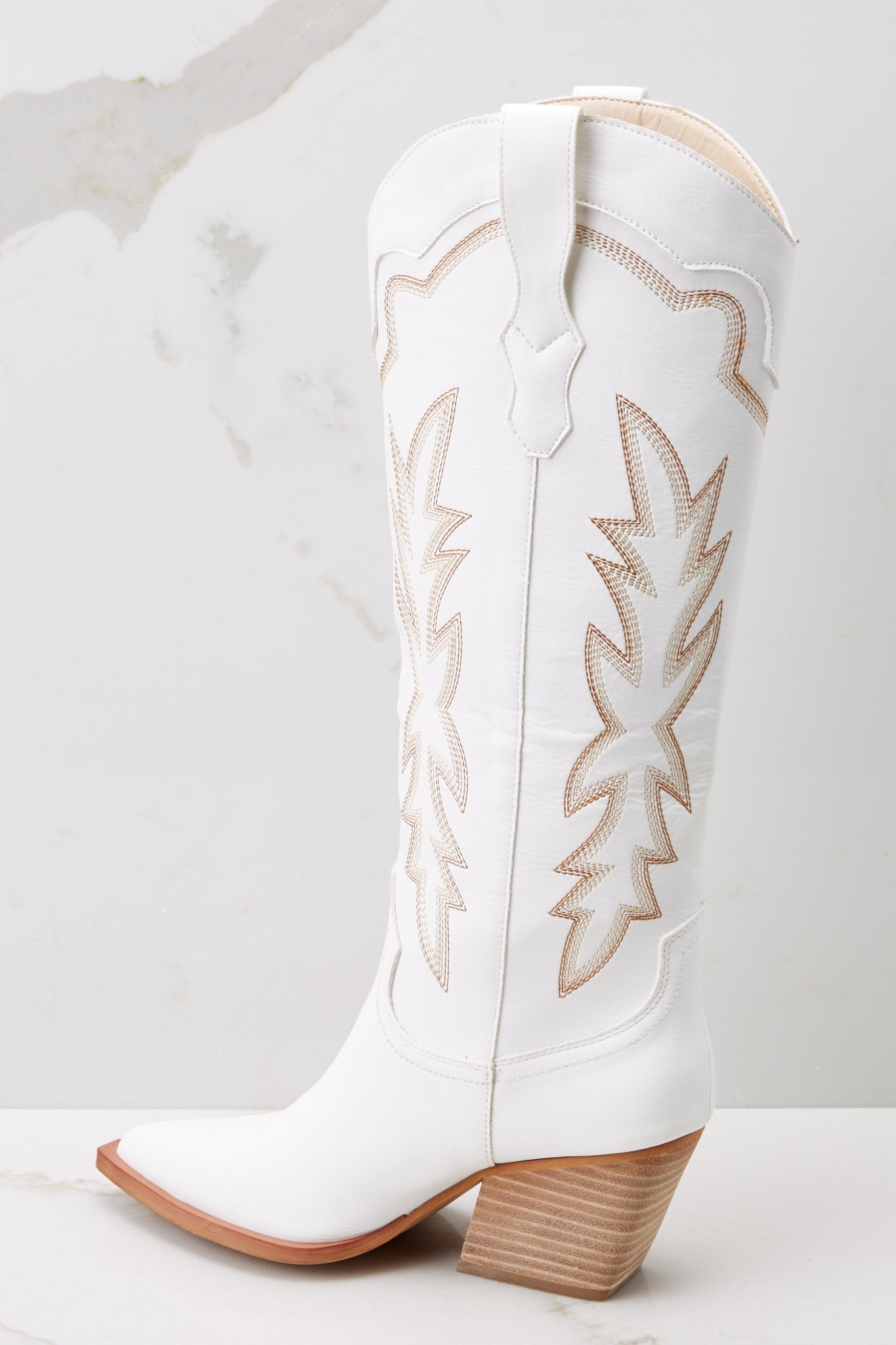Inner-side view of these boots that feature a pointed toe and tan stitched design up the leg.