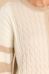Close up view of this cable knit sweater that features a scoop neckline and a color block design.