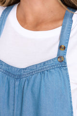 Close up view of these overalls that feature a slight scoop neckline and thin shoulder straps with button closures.