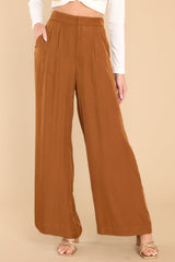 These brown pants feature a high rise, a zipper and hook and eye closure, an elastic band at the back of the waist, functional pockets, and a wide leg.