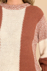 Close up view of this sweater that features a round neckline, long sleeves with stretchy cuffs, a chunky knit texture, and a striped colorblock design.