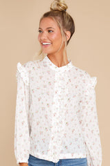 This ivory floral top features buttons and ruffles down the front and sleeves with elastic cuffs.