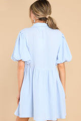 Back view of  this dress that features a collared neckline, functional buttons down the front, puff sleeves with elastic cuffs, functional waist pockets, and a flowy skirt.