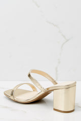 Inner-side view of these high heel sandals that feature a square toe, beige insole, two matching gold straps, and a matching color heel. 