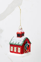 Side view of this ornament that features a barn shape with a green roof and a wreath on the door with gold accents.