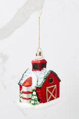 Back view of this ornament that features a barn shape with a green roof and a wreath on the door with gold accents.