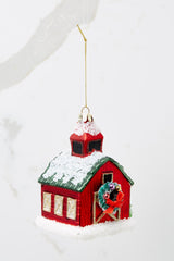 This red ornament features a barn shape with a green roof and a wreath on the door with gold accents.
