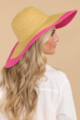 This tan hat features a wide brim, woven material, and a pink color detail along the brim.