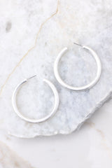 Detailed view of hoop earrings that feature a slightly matte finish, silver hardware, and a secure post backing.