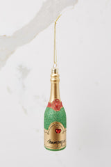 This green champagne bottle ornament features red and green glitter with gold accents and  a gold string for hanging.
