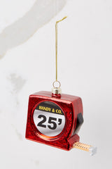 This red ornament features a red measuring tape with a gold string to hang on the tree.