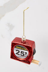 Top view of this ornament that features a red measuring tape with a gold string to hang on the tree