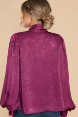 Back view of this top that features a high neckline with an adjustable self tie, flowy balloon sleeves with two buttons at the cuff, and a relaxed fit.