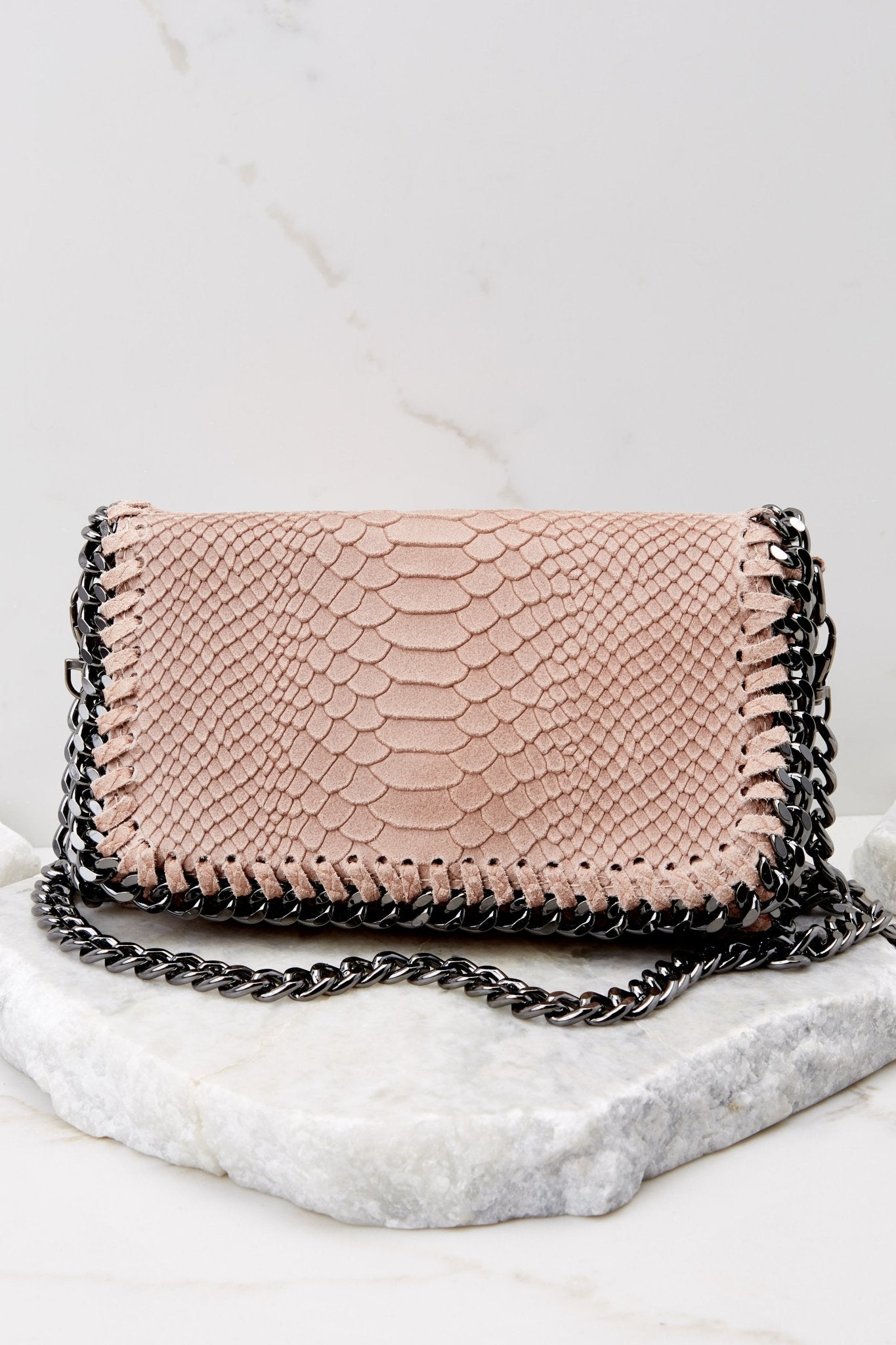 This light pink bag features faux snakeskin, a front flap opening with a silver metal magnetic closure, and a chain strap.