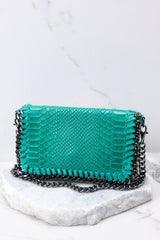 This green bag features faux snakeskin, a front flap opening with a silver metal magnetic closure, a chain strap. 