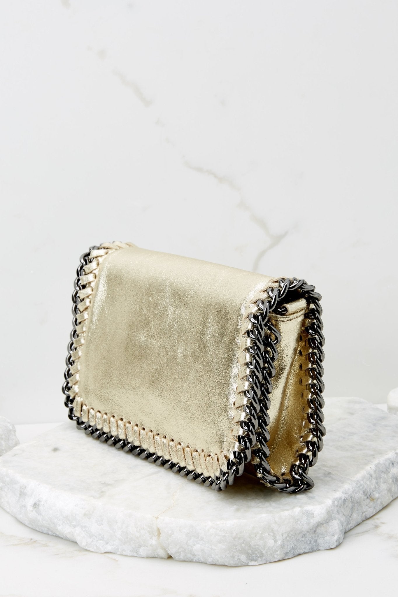 Angled side view of this clutch that features a front flap that has a silver magnetic closure, an inside zipper, a removable leather strap, and wide decorative stitching around the edges.