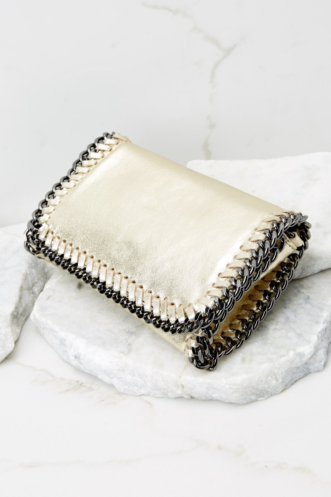 Side view of this clutch that features a front flap that has a silver magnetic closure, an inside zipper, a removable leather strap, and wide decorative stitching around the edges. 