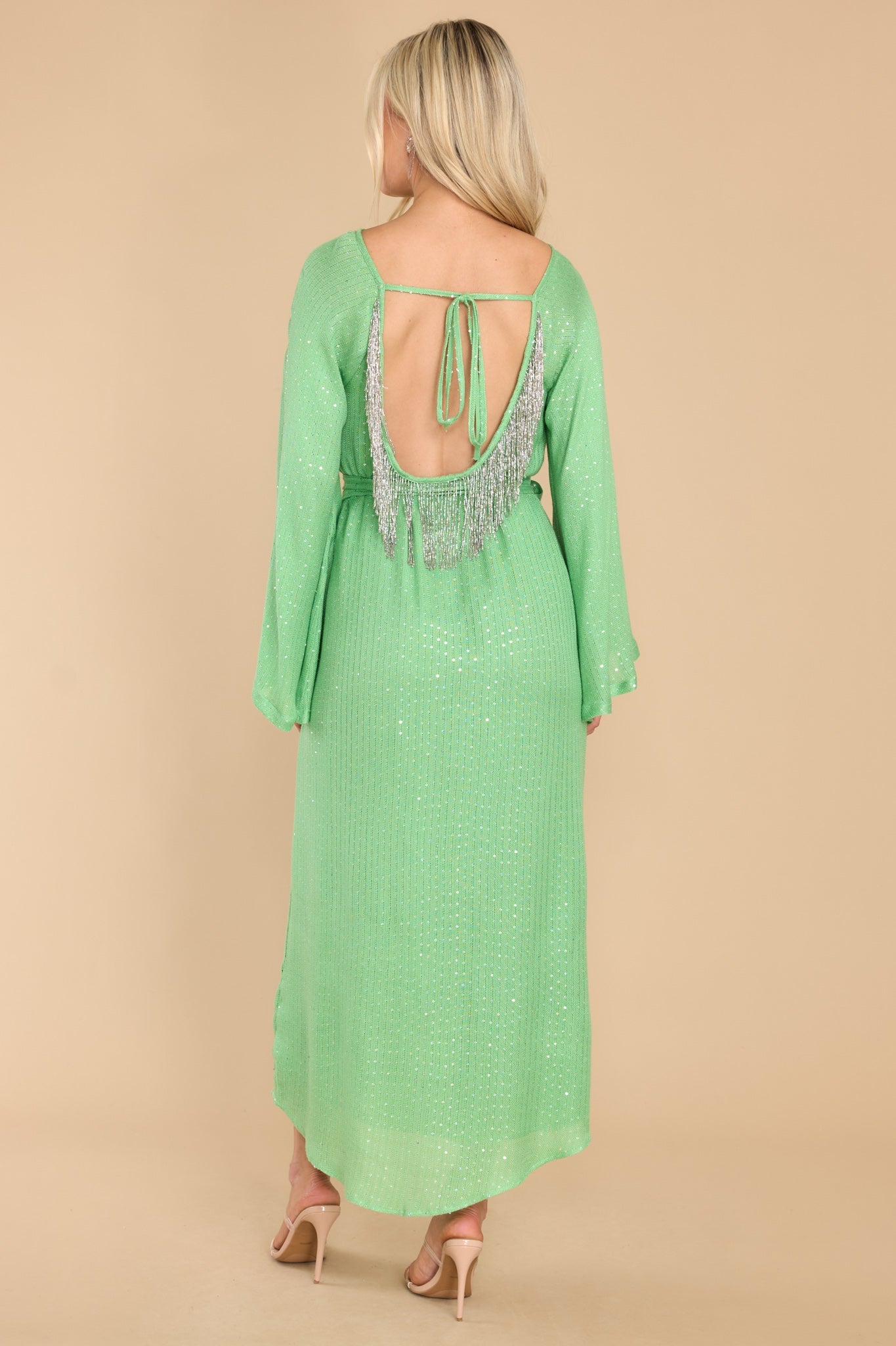 This  green dress features a high neckline, an open back with a self-tie, sequins throughout, beaded fringe detailing at the back, and an optional tie belt.