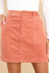 Close up view of this skirt that features a button and zipper closure, belt loops, two functional square pockets, and a velvety corduroy material throughout. 
