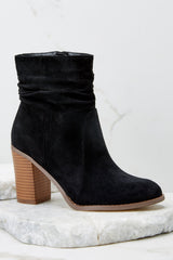 These black vegan suede booties feature a round toe, slouchy ankle detail, stitching around the base, functional side zipper, and a thick wood-inspired stacked heel.