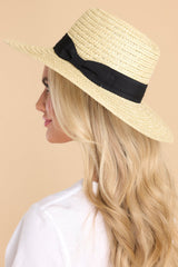 Side view of this hat that features a straw design and a black ribbon around the base of the hat.