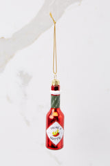 This red ornament features a design of a hot sauce bottle with glitter accents and 