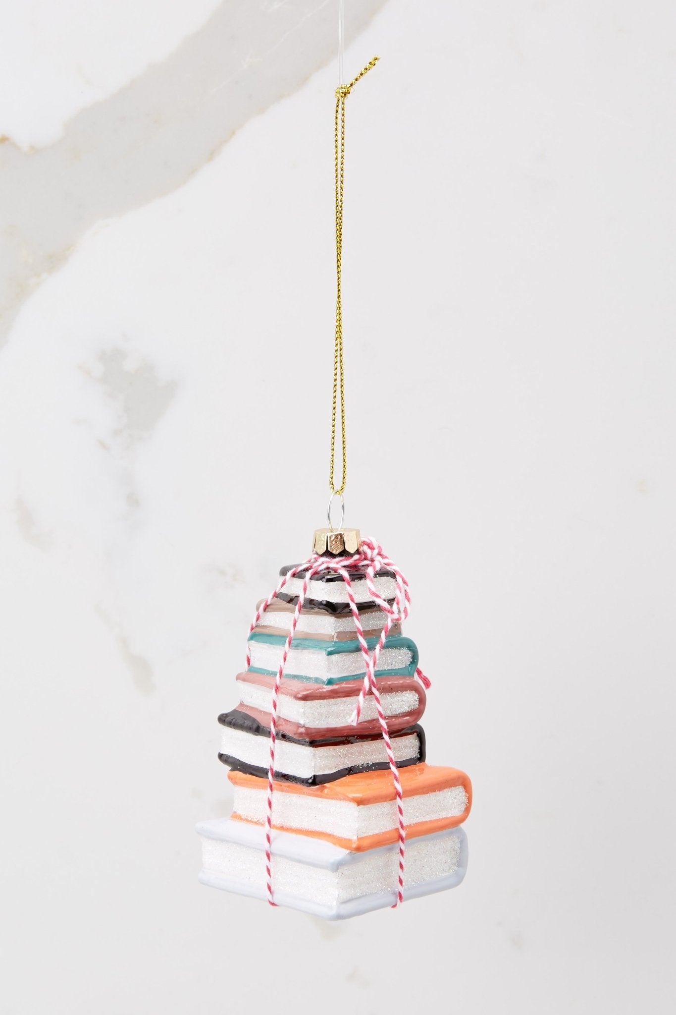 Back view of this ornament that features a design of stacked books with glitter accents and striped string.
