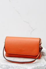 This orange crossbody bag is made with real leather, has two detachable straps; one is a short matching leather strap, and the other is a curb chain crossbody strap, a magnetic snap closure, and measures 8