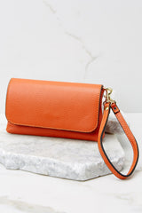 Full view of this orange crossbody bag that is made with real leather, has two detachable straps; one is a short matching leather strap, and the other is a curb chain crossbody strap, a magnetic snap closure, and measures 8