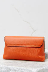 Back view of this orange crossbody bag that is made with real leather, has two detachable straps; one is a short matching leather strap, and the other is a curb chain crossbody strap, a magnetic snap closure, and measures 8