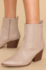 These taupe ankle boots feature a pointed toe, a side zipper closure, a stretchy side panel, and a stacked heel. 