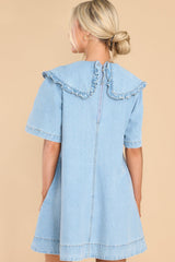 Back view of this dress that features a high neckline with a ruffled collar, short sleeves functional zipper in the back, pockets, and chambray design.