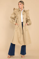 This camel colored coat features a collar neckline, ruffle detailing along the shoulders and bust area, puff sleeves with buttoned cuffs, a self-tie around the waist for a custom fit, and two functional waist pockets.