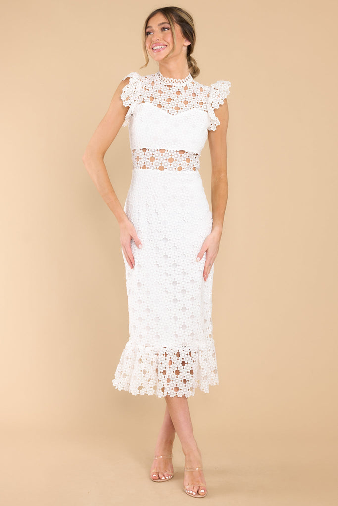 This all white crochet lace midi dress features a high neckline with an illusion sweetheart neckline, ruffled shoulders, a peek-a-boo waistline which gives way into a sheath silhouette fit, and a flounced hem. Dress has a visible back zipper. 