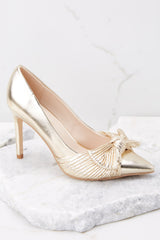Outside view of gold high heels featuring a skinny heel and closed toe. 