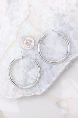 Overhead view of hoops that feature a silver design and a post-back closure compared to quarter for actual size. 