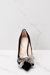 Front view of black heels with a silver bow detail and closed toes. 