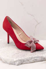 Outer-side view of these heels that feature a red suede detail throughout the shoe with rhinestone covered bow and pointed toe.