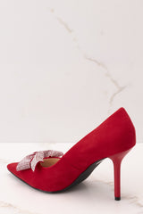 Inner-side view of these heels that feature a red suede detail throughout the shoe with rhinestone covered bow and pointed toe.