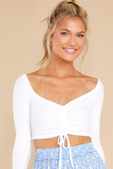 This all white crop top features a scrunched center complimented by an adjustable self tie, a lower scoop neck, and a ribbed fabric.