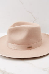 This nude colored hat features a teardrop crown with a stiff upturned brim and a band around the crown.