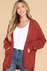 This rust colored cardigan features a soft, chunky knit design, functional pockets, and small slits up the sides.