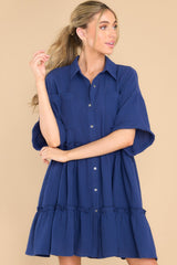 Front view of  this dress that features a collared neckline, functional buttons down the front, functional pockets at the bust, short sleeves with folded cuffs, and ruffle detailing throughout the skirt.
